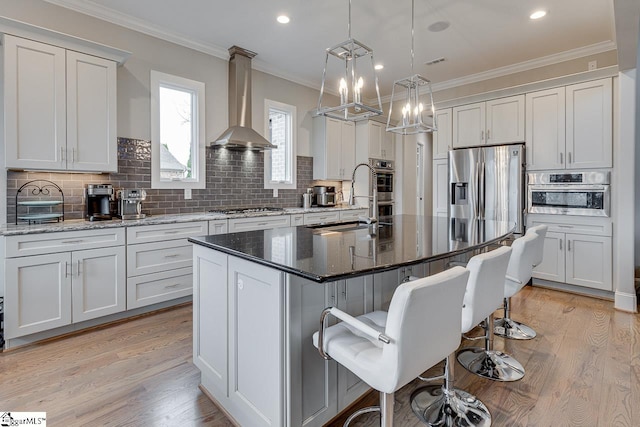 kitchen with an island with sink, wall chimney range hood, white cabinetry, and a breakfast bar