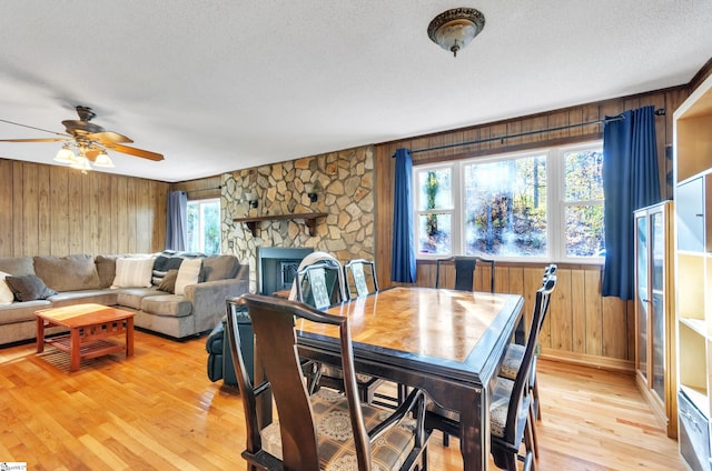 dining space featuring a stone fireplace, wooden walls, plenty of natural light, and light wood-type flooring