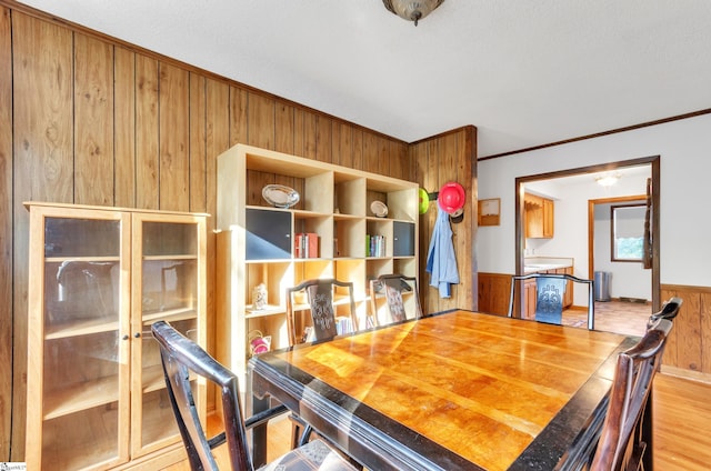 dining area with wood walls, light hardwood / wood-style flooring, and ornamental molding