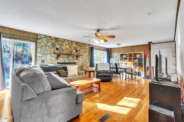 living room featuring a textured ceiling, hardwood / wood-style flooring, ceiling fan, and wooden walls