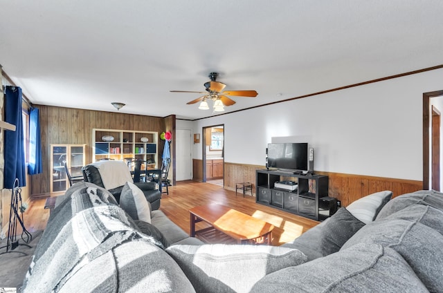 living room featuring ceiling fan, wood walls, wood-type flooring, and ornamental molding