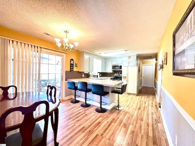 kitchen featuring white cabinets, kitchen peninsula, appliances with stainless steel finishes, decorative light fixtures, and backsplash