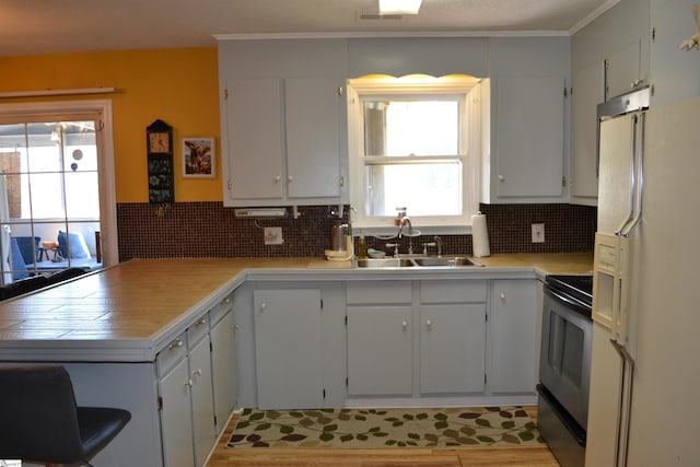 kitchen featuring white refrigerator with ice dispenser, sink, kitchen peninsula, black electric range, and white cabinetry