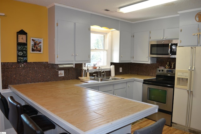 kitchen featuring sink, kitchen peninsula, backsplash, white cabinetry, and stainless steel appliances