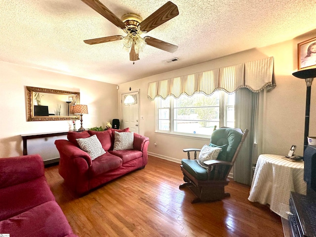 living room featuring hardwood / wood-style flooring, ceiling fan, and a textured ceiling