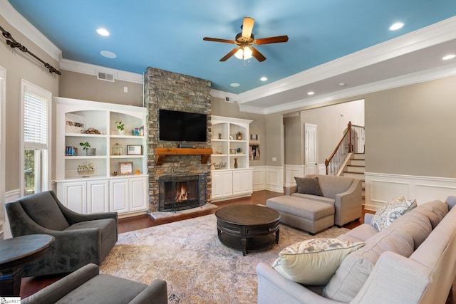 living room with crown molding, ceiling fan, a stone fireplace, and light hardwood / wood-style flooring