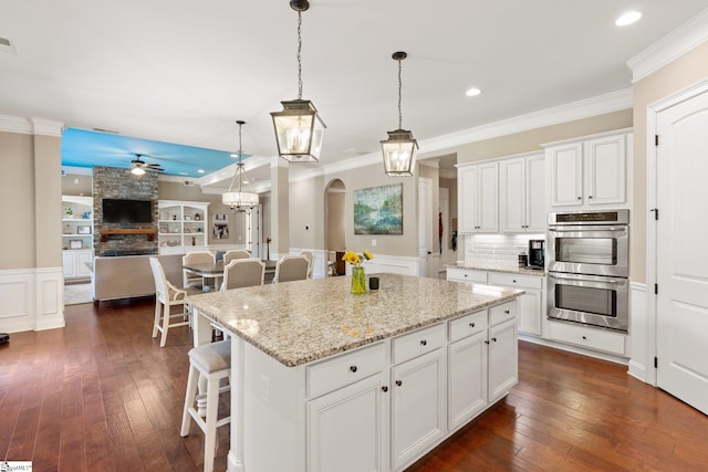 kitchen with stainless steel double oven, a kitchen island, a kitchen bar, and white cabinetry