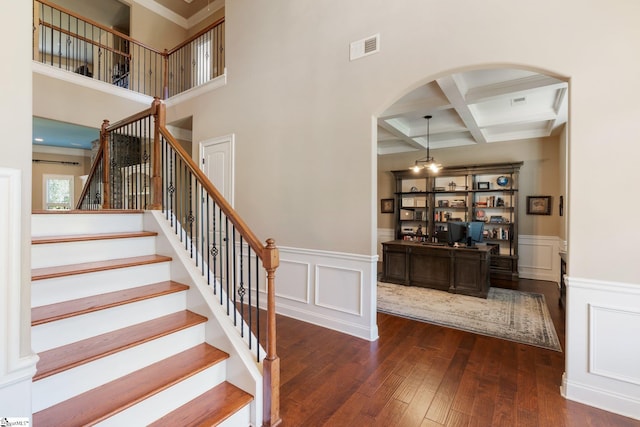 stairs with hardwood / wood-style flooring, coffered ceiling, a towering ceiling, ornamental molding, and beam ceiling