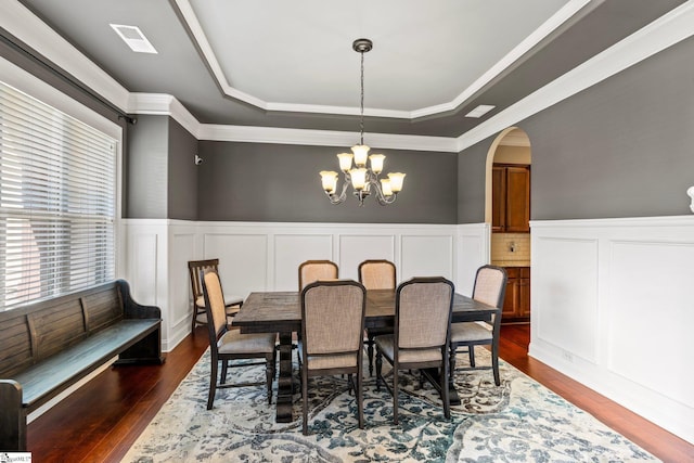 dining area with an inviting chandelier, a raised ceiling, dark hardwood / wood-style floors, and crown molding