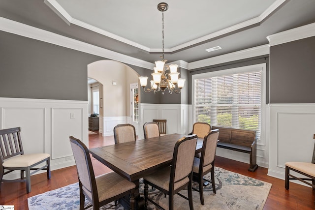 dining space featuring dark wood-type flooring, a raised ceiling, crown molding, and an inviting chandelier