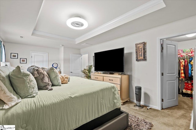 bedroom with a spacious closet, crown molding, a tray ceiling, and light colored carpet