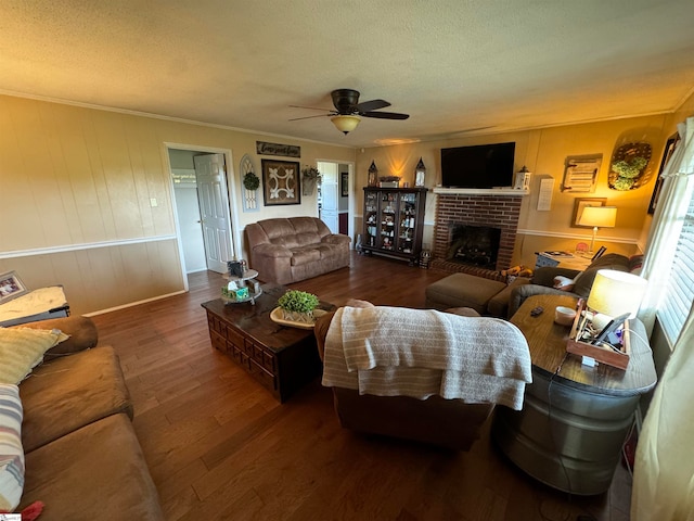 living room featuring ceiling fan, dark hardwood / wood-style flooring, a brick fireplace, a textured ceiling, and ornamental molding