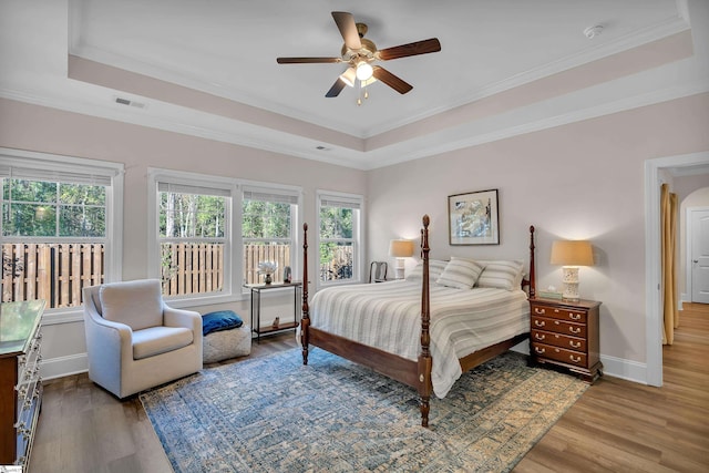 bedroom with a raised ceiling, wood-type flooring, ornamental molding, and ceiling fan