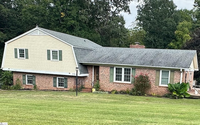split level home featuring a front yard, a shingled roof, and brick siding