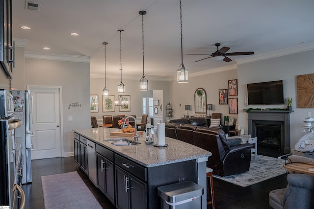 kitchen with sink, dark hardwood / wood-style floors, light stone counters, a center island with sink, and decorative light fixtures