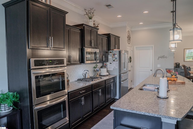 kitchen with sink, a kitchen island with sink, backsplash, stainless steel appliances, and light stone counters