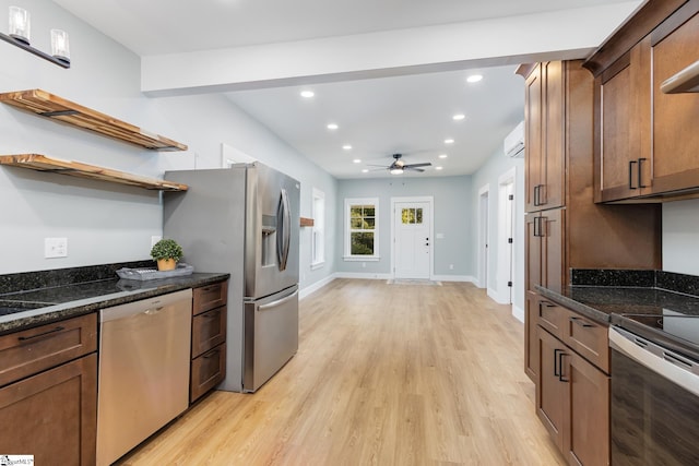 kitchen featuring a wall mounted AC, light hardwood / wood-style flooring, stainless steel appliances, dark stone counters, and ceiling fan