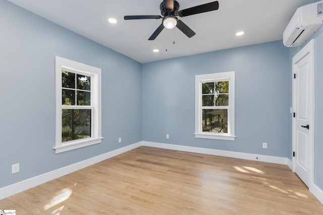 spare room featuring an AC wall unit, light wood-type flooring, and ceiling fan