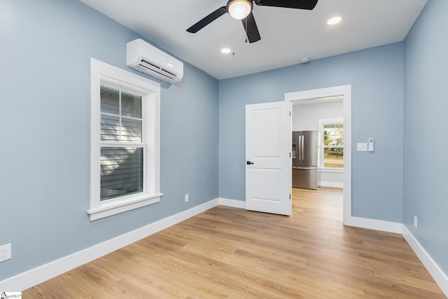 unfurnished room featuring a wall unit AC, light wood-type flooring, and ceiling fan