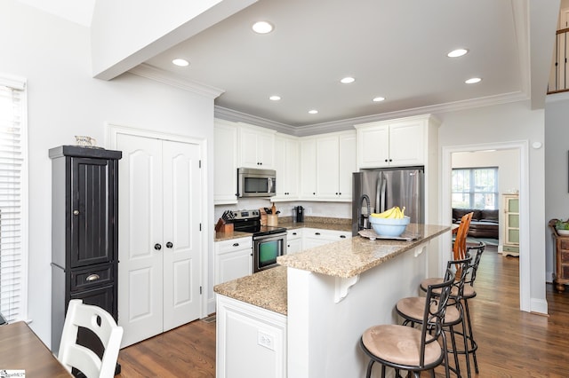 kitchen with light stone countertops, appliances with stainless steel finishes, white cabinetry, a breakfast bar area, and a center island with sink