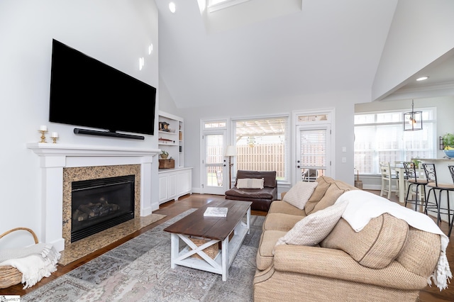 living room with a premium fireplace, built in shelves, wood-type flooring, and high vaulted ceiling