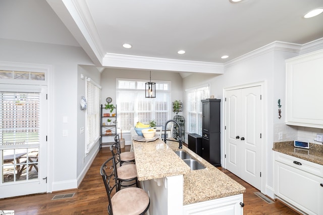 kitchen with a kitchen island with sink, hanging light fixtures, a breakfast bar, light stone countertops, and dark hardwood / wood-style flooring