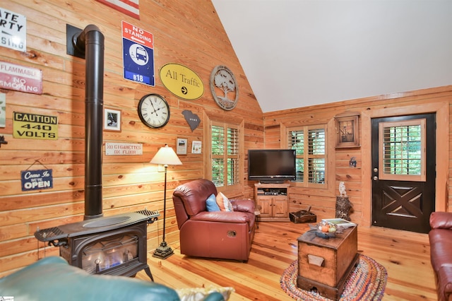 living room with a wood stove, wood walls, hardwood / wood-style flooring, and high vaulted ceiling