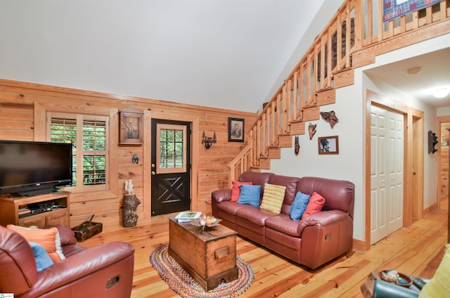 living room featuring wood walls, lofted ceiling, and light wood-type flooring