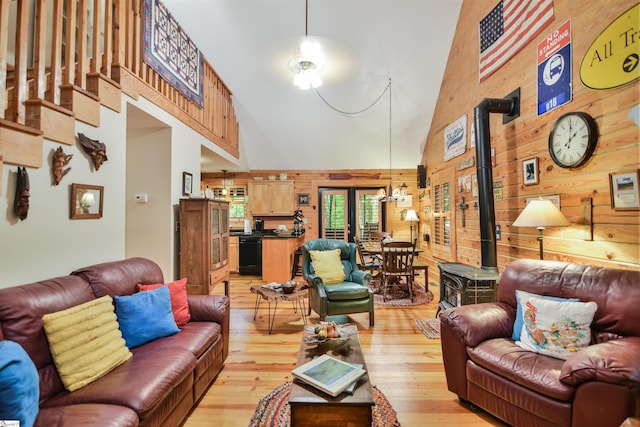 living room with light hardwood / wood-style floors, a wood stove, wood walls, and high vaulted ceiling