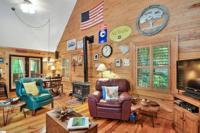 living room with wooden walls, light hardwood / wood-style flooring, high vaulted ceiling, and a wood stove