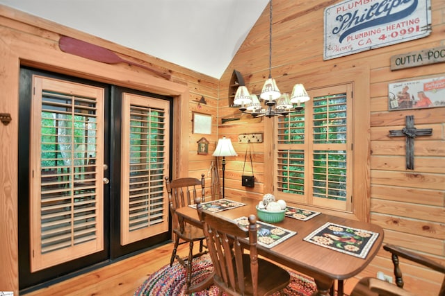 dining area featuring wood-type flooring, lofted ceiling, wooden walls, and an inviting chandelier