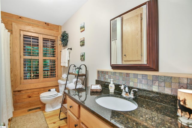 bathroom with vanity, wood-type flooring, toilet, and tasteful backsplash