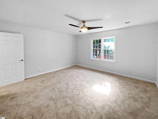 carpeted empty room with visible vents, a ceiling fan, and baseboards