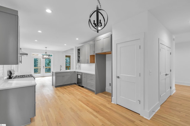 kitchen with gray cabinetry, sink, wall chimney exhaust hood, decorative light fixtures, and decorative backsplash