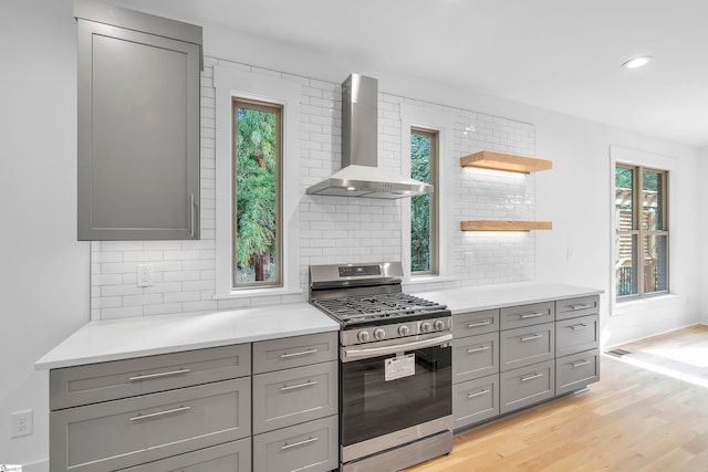 kitchen with stainless steel gas stove, wall chimney range hood, light wood-type flooring, and a healthy amount of sunlight