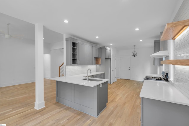 kitchen featuring stainless steel range, kitchen peninsula, sink, light wood-type flooring, and gray cabinets