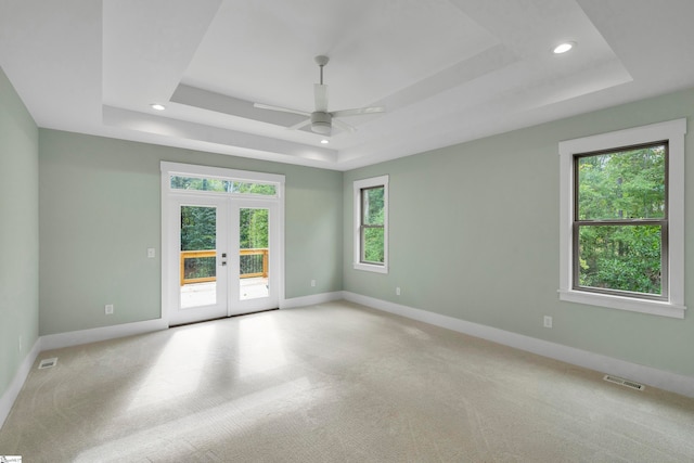 carpeted spare room featuring french doors, a tray ceiling, and ceiling fan