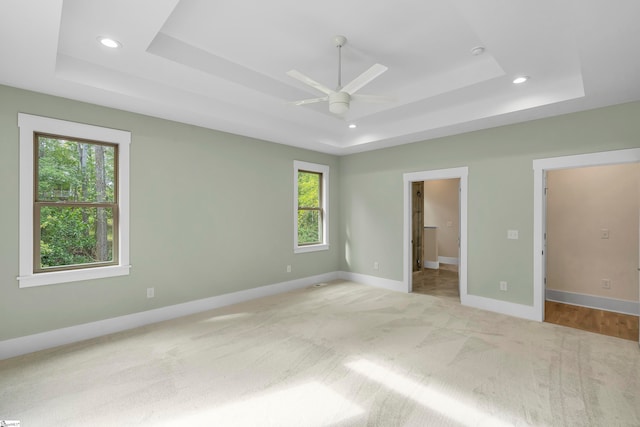 unfurnished bedroom featuring a raised ceiling, light carpet, and ceiling fan