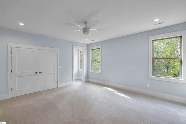 unfurnished bedroom featuring a closet, multiple windows, light colored carpet, and ceiling fan