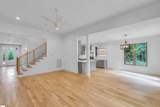 unfurnished living room featuring ceiling fan with notable chandelier and light wood-type flooring