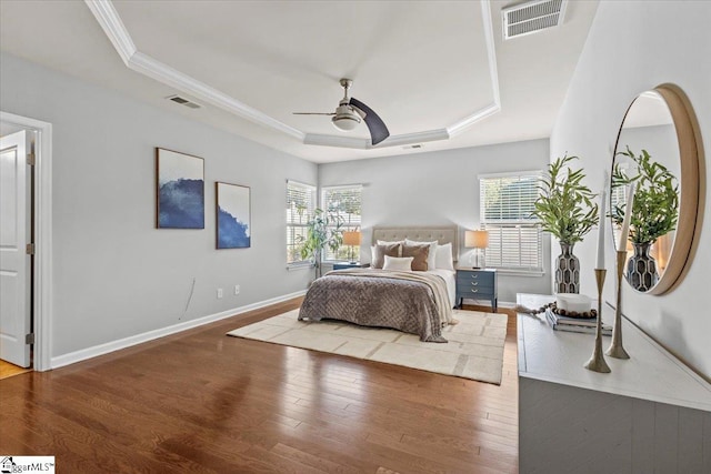 bedroom featuring hardwood / wood-style floors, multiple windows, a tray ceiling, and ceiling fan