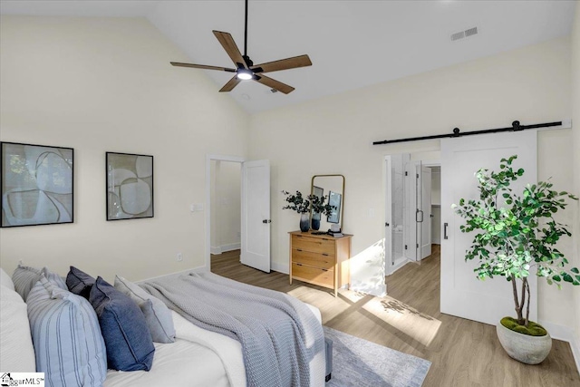 bedroom with ceiling fan, high vaulted ceiling, light hardwood / wood-style floors, and a barn door