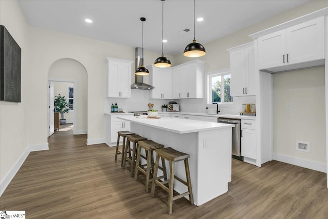 kitchen featuring wall chimney range hood, a kitchen island, white cabinetry, dishwasher, and pendant lighting