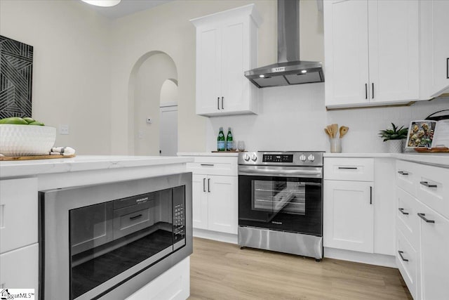 kitchen with white cabinets, black microwave, stainless steel electric range oven, light wood-type flooring, and wall chimney exhaust hood