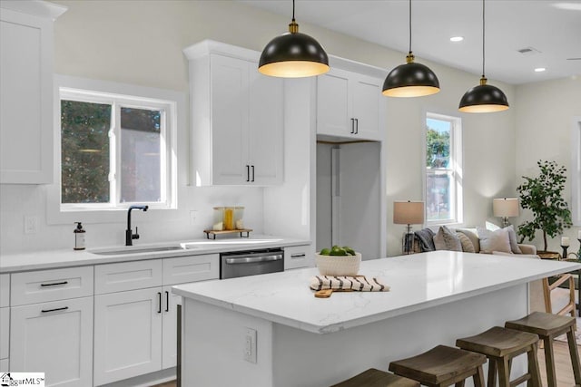 kitchen with sink, a breakfast bar, pendant lighting, stainless steel dishwasher, and white cabinetry