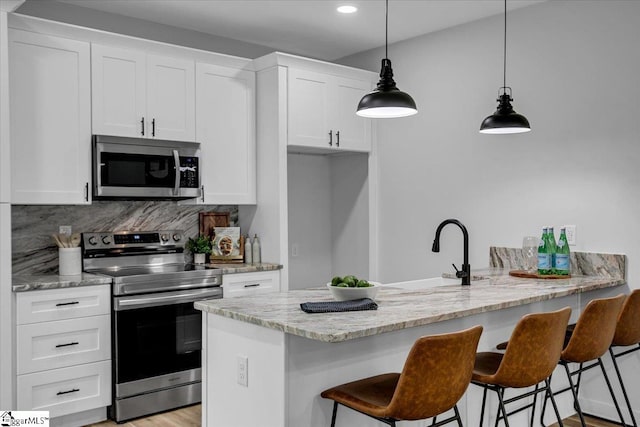 kitchen featuring white cabinetry, light stone counters, appliances with stainless steel finishes, and pendant lighting