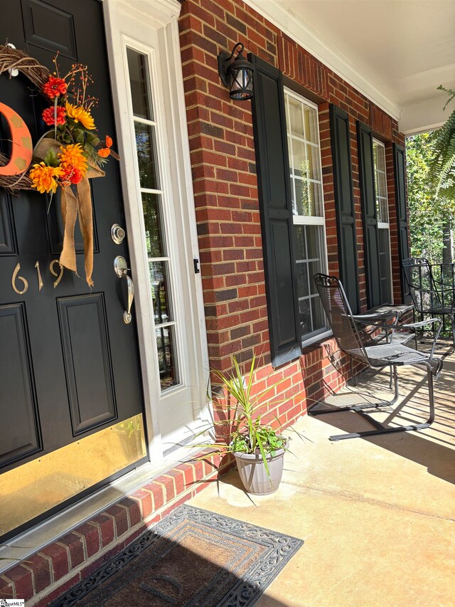 doorway to property featuring covered porch and brick siding