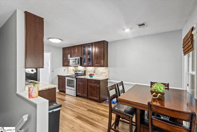 kitchen with tasteful backsplash, a textured ceiling, dark brown cabinets, light hardwood / wood-style floors, and stainless steel appliances