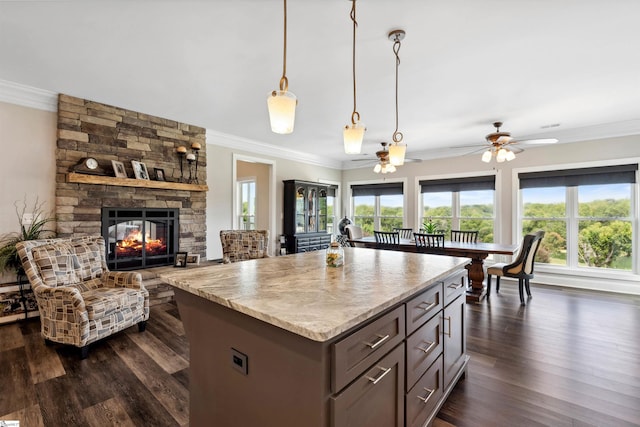 kitchen featuring hanging light fixtures, ceiling fan, dark hardwood / wood-style flooring, ornamental molding, and a fireplace