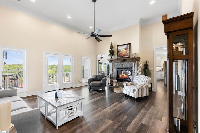 living room featuring a high ceiling, a stone fireplace, dark hardwood / wood-style floors, ornamental molding, and ceiling fan